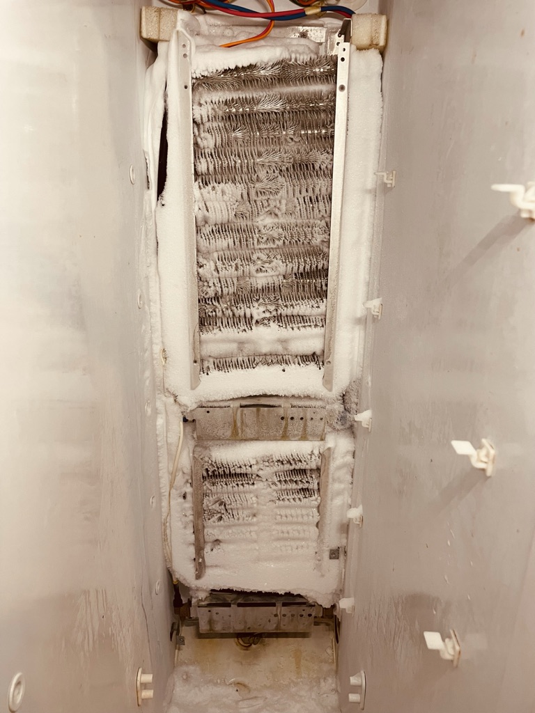 Refrigerator technician inspecting condenser coils for repair in Charlotte, NC.